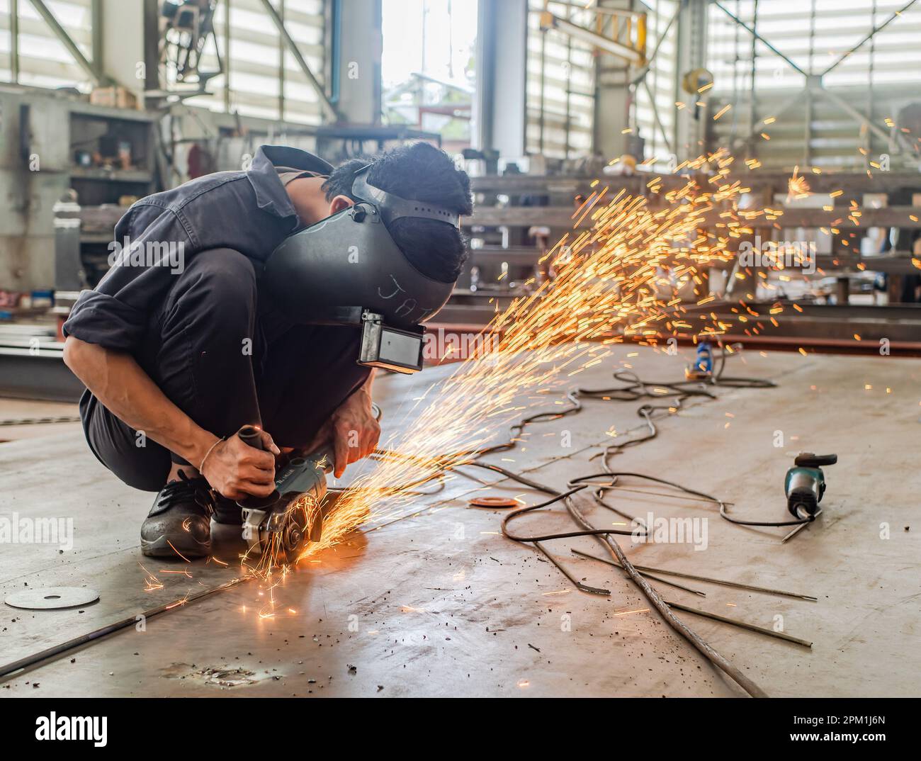Un lavoratore industriale maschile che indossa una maschera di saldatura utilizzando una smerigliatrice angolare su una piastra di acciaio, scintille che volano. Foto Stock
