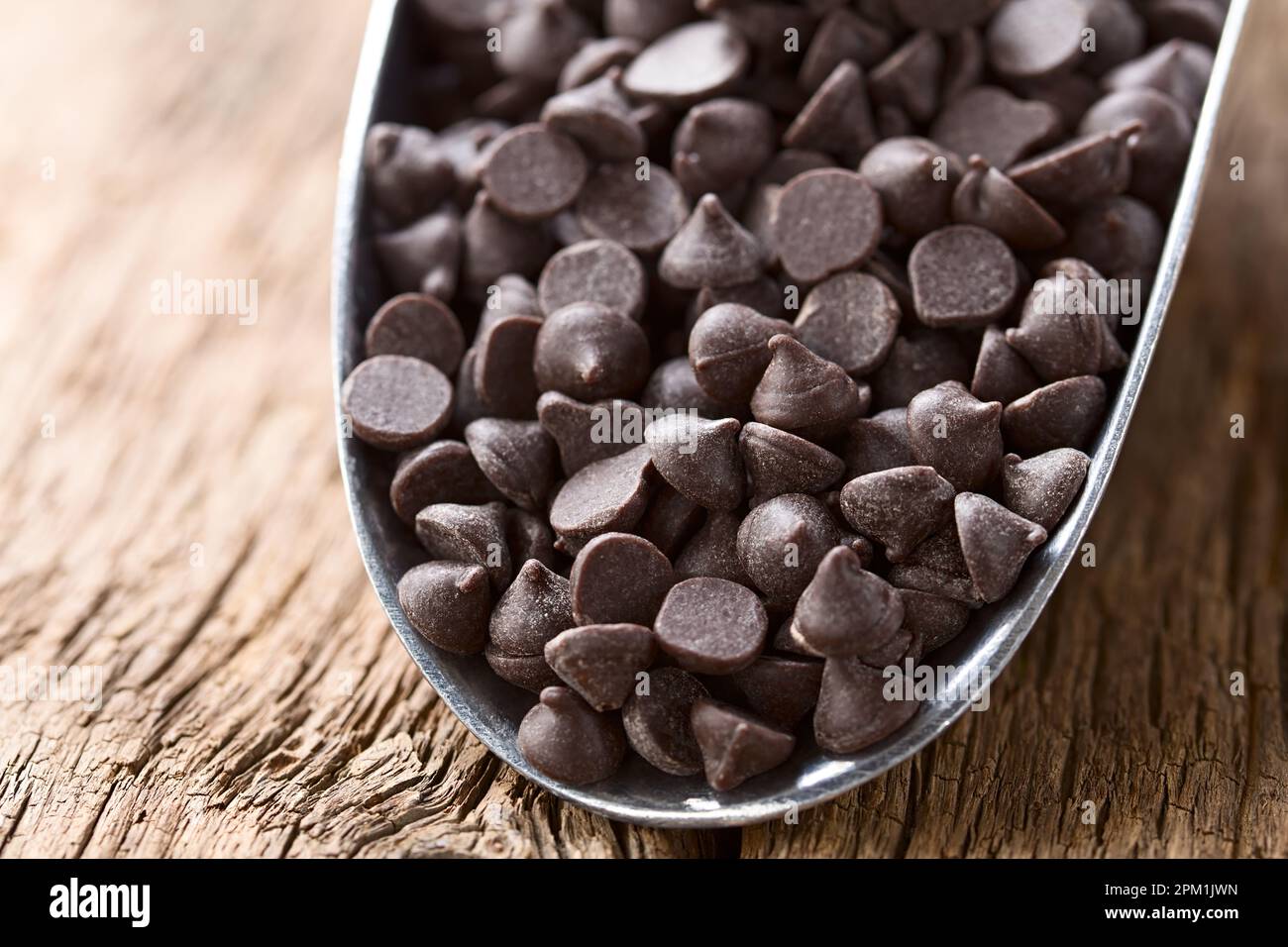 Gocce di cioccolato o bocconcini in metallo su legno (fuoco selettivo, focalizzazione di un terzo nelle gocce di cioccolato) Foto Stock