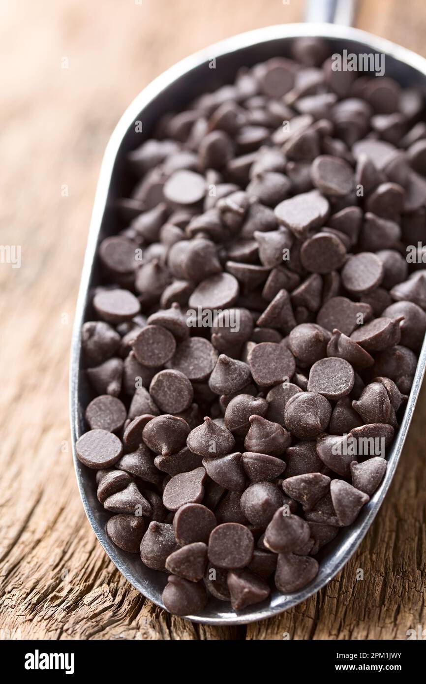 Gocce di cioccolato o bocconcini in metallo su legno (fuoco selettivo, focalizzazione di un terzo nelle gocce di cioccolato) Foto Stock