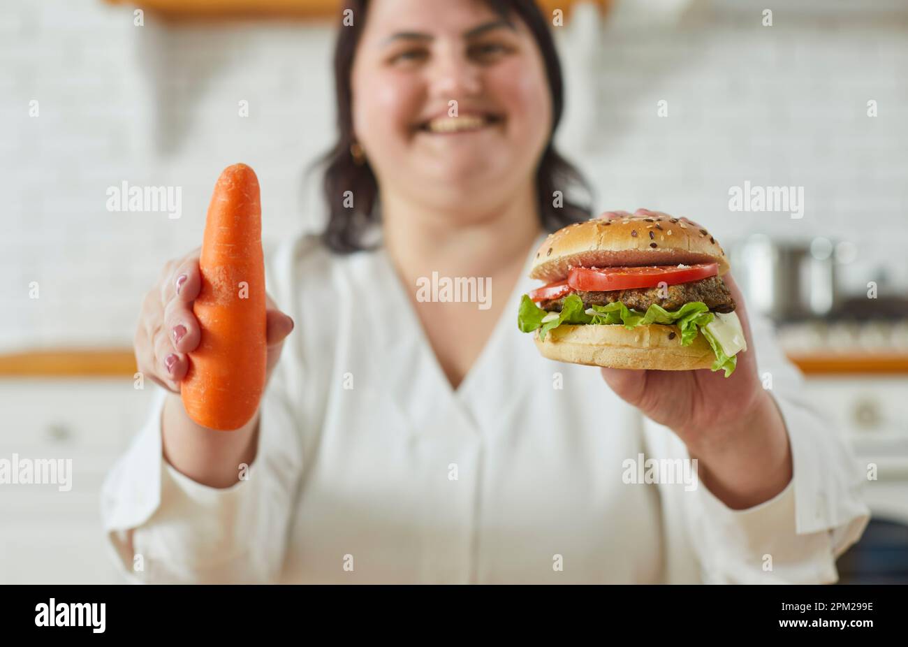 Giovane donna grassa di peso maggiorato che tiene un hamburger in una mano e una carota in un'altra. Foto Stock