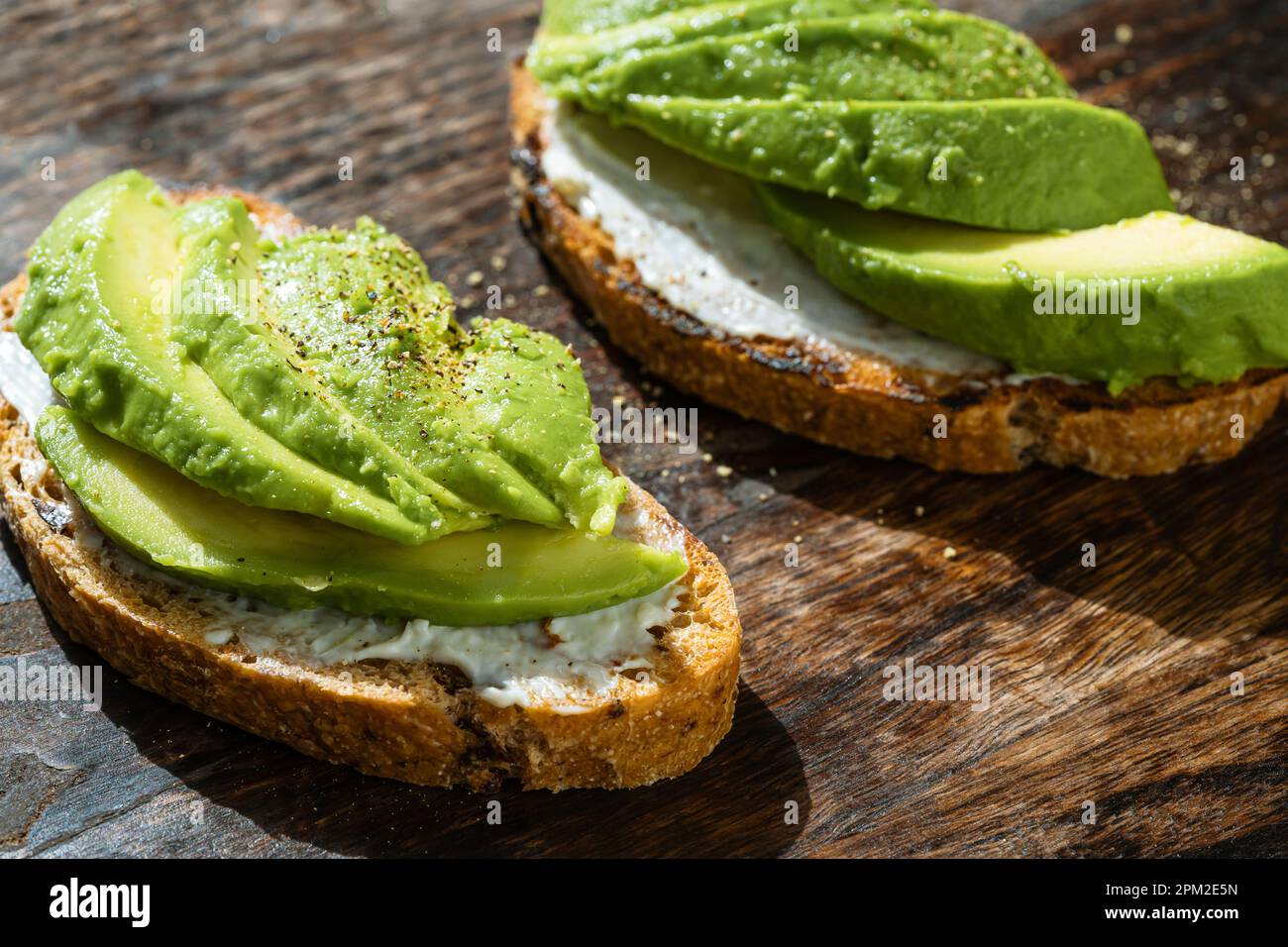Due toast di grano integrale con fettine di avocado su un rustico asse di legno. Cibo messicano, primo piano Foto Stock