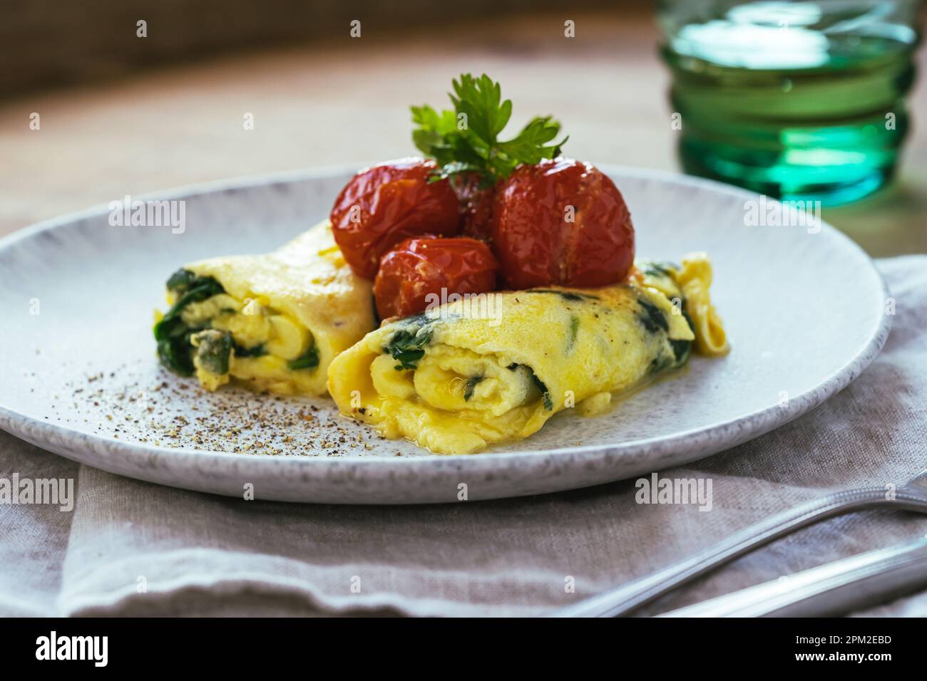 Frittata fatta in casa con spinaci e pomodori ciliegini arrosto in piatto di ceramica su tavolo rustico in legno, sana colazione frittata francese con verdure Foto Stock