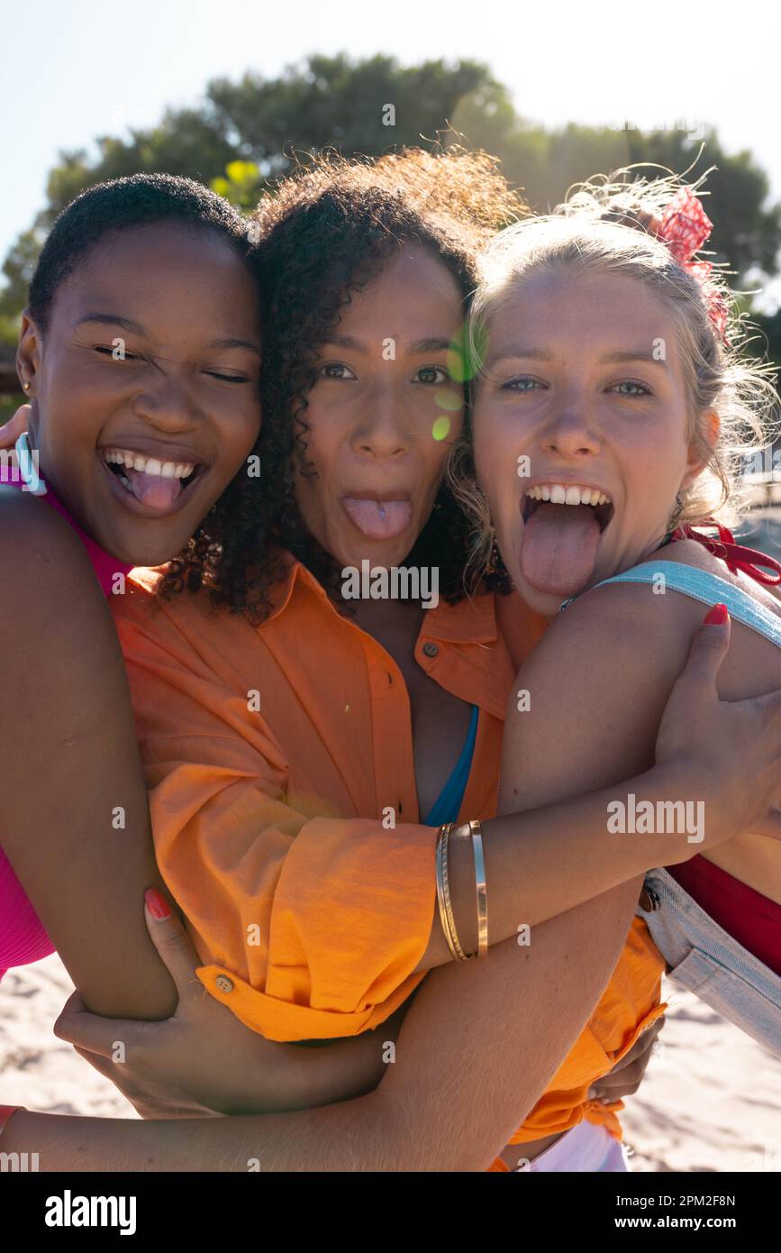 Ritratto di felici e diversi amici femminili abbracciando e attaccando la lingua fuori in spiaggia, con spazio copia Foto Stock