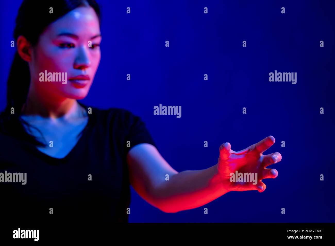 Donna asiatica che fa un gesto con mano in studio con luce blu con spazio copia Foto Stock