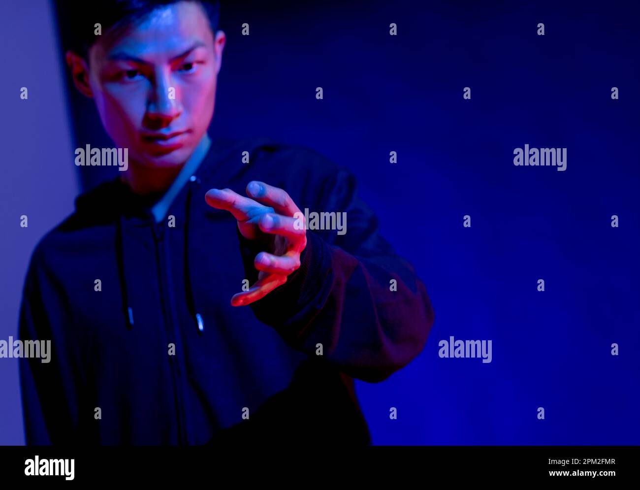 Uomo asiatico che fa un gesto a mano in studio con luce blu con spazio copia Foto Stock