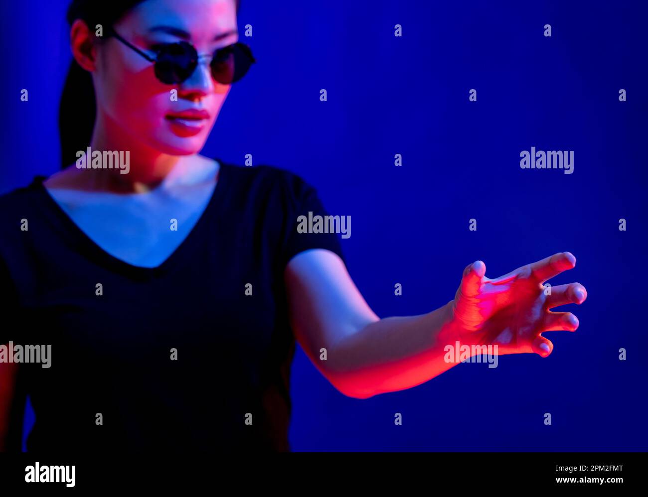 Donna asiatica con occhiali facendo gesto a mano in studio con luce blu con spazio copia Foto Stock