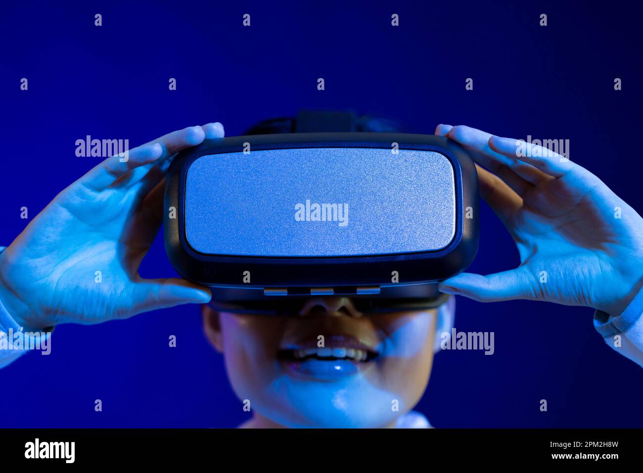 Ritratto di donna asiatica che tiene il visore vr in studio con luce blu Foto Stock