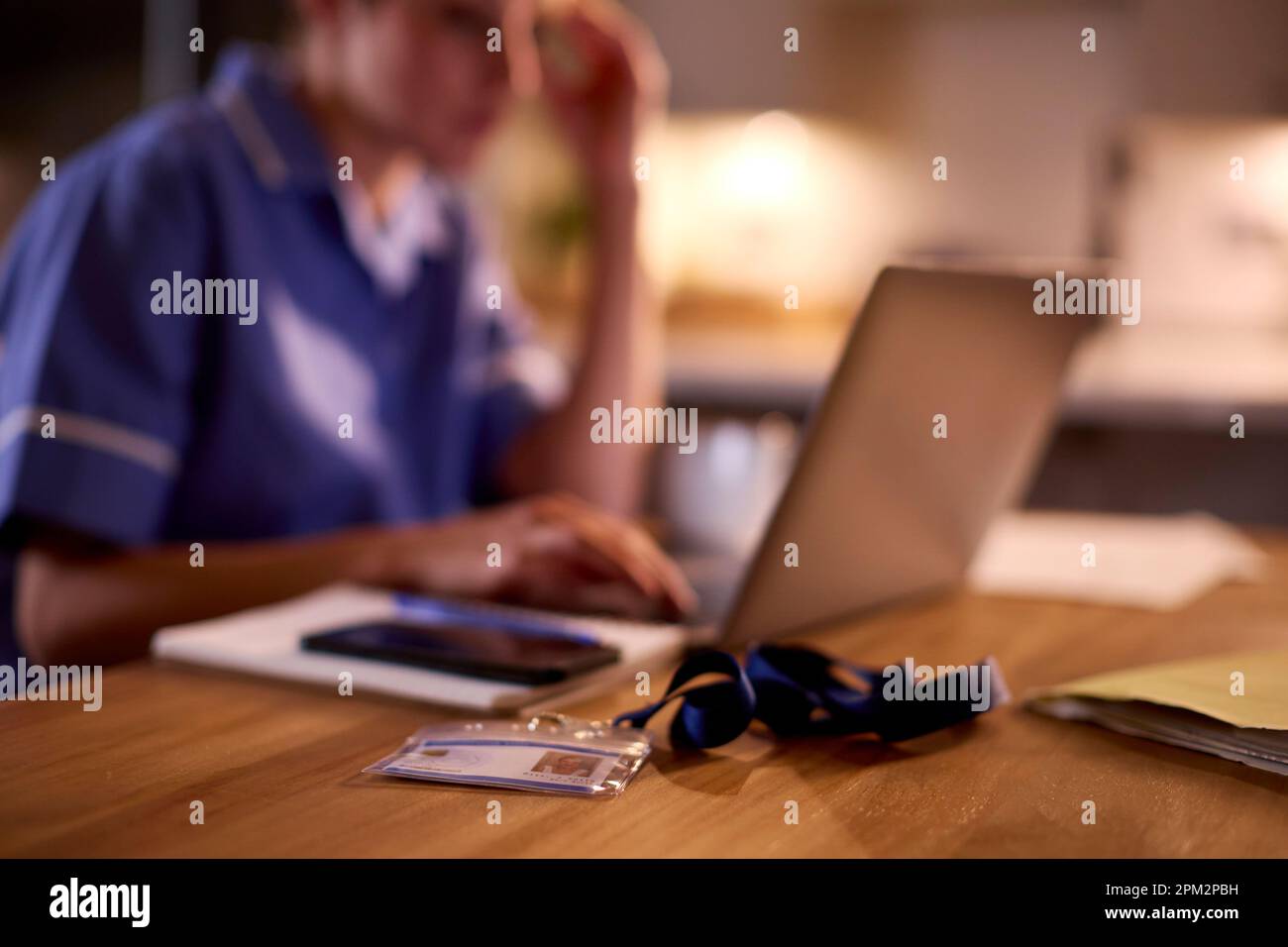 Donna in uniforme medica che lavora o studia sul portatile a casa di notte con il cordone di sicurezza ID Foto Stock