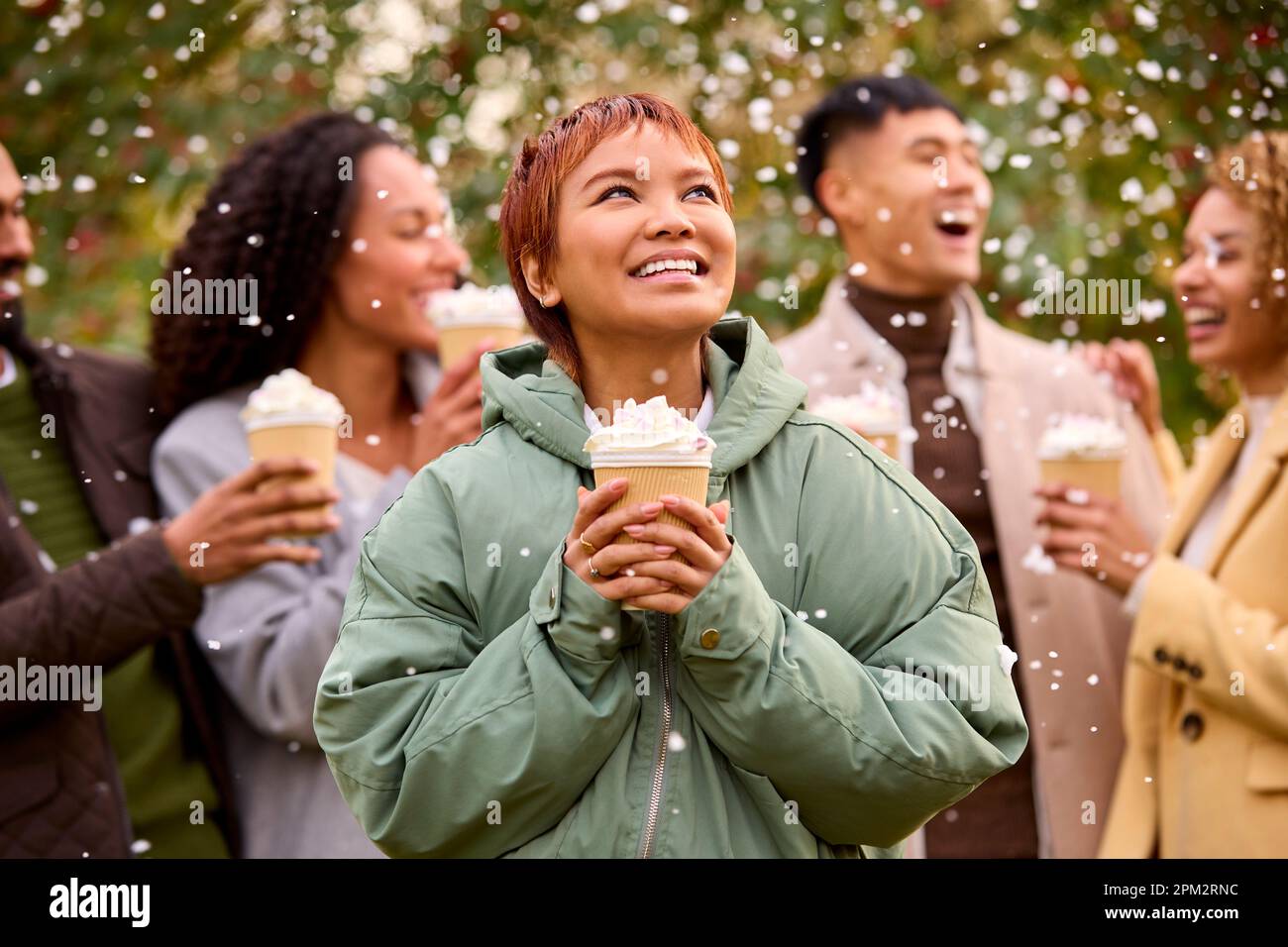 Gruppo di amici che indossano cappotti in piedi all'esterno in Snow Holding bevande calde al cioccolato Foto Stock