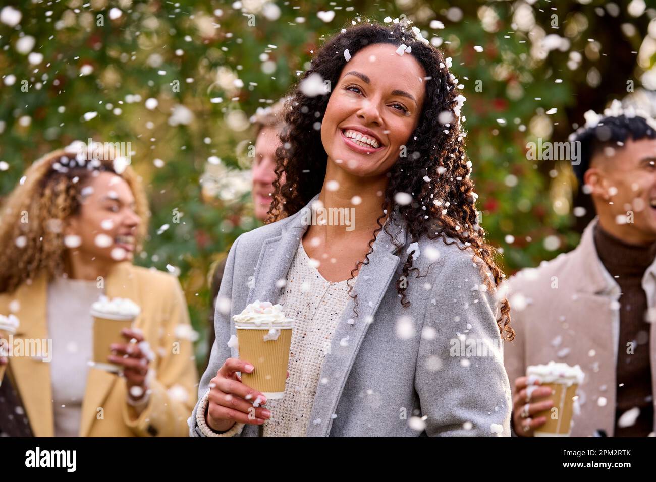 Gruppo di amici che indossano cappotti in piedi all'esterno in Snow Holding bevande calde al cioccolato Foto Stock