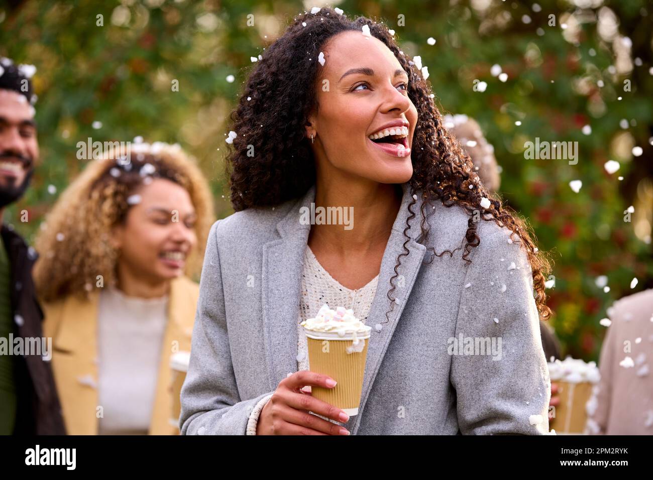 Gruppo di amici che indossano cappotti in piedi all'esterno in Snow Holding bevande calde al cioccolato Foto Stock