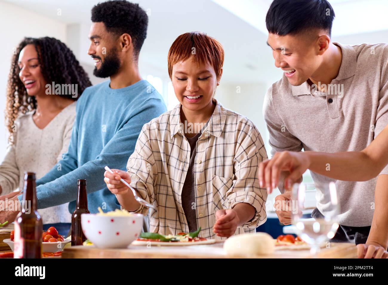 Gruppo di amici a casa in cucina aggiungendo condimenti alle pizze fatte in casa per la festa insieme Foto Stock