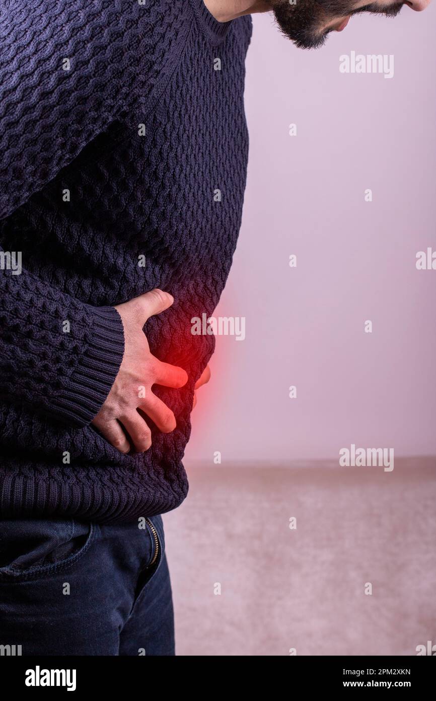 Uomo che soffre con grave dolore allo stomaco seduto a casa. Mano del tipo maturo che tiene l'addome che soffre dal dolore, dalla diarrea o dal problema indigestive. Paint Foto Stock