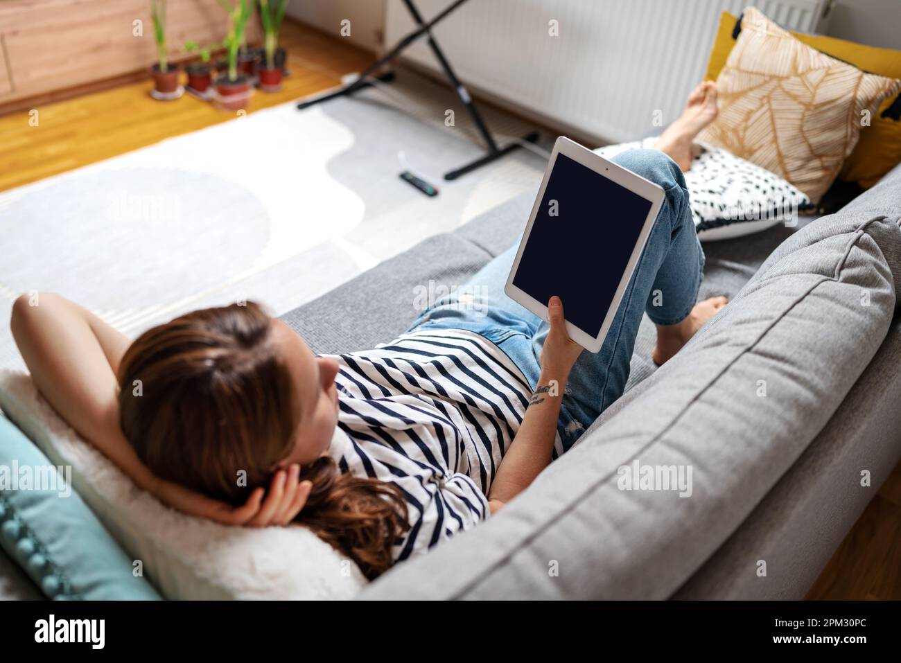 Donna sdraiata sul divano a casa e riedendo ebook. Foto Stock