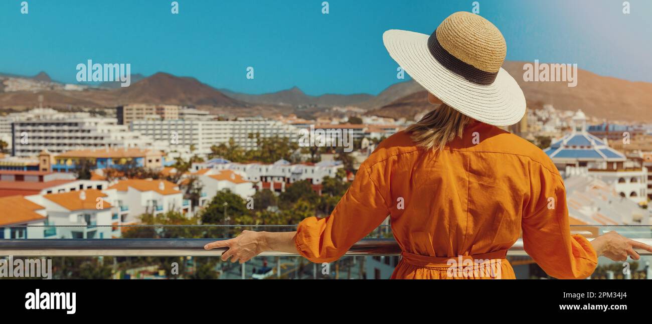 Donna in piedi sul balcone e che gode di vista sullo skyline del resort di vacanza Playa de las Americas a Tenerife. banner con spazio di copia Foto Stock