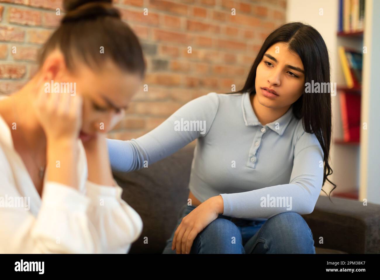 Signora spagnola che sostiene e calmando la sua amica che ha problemi, seduta sul divano e parlando Foto Stock