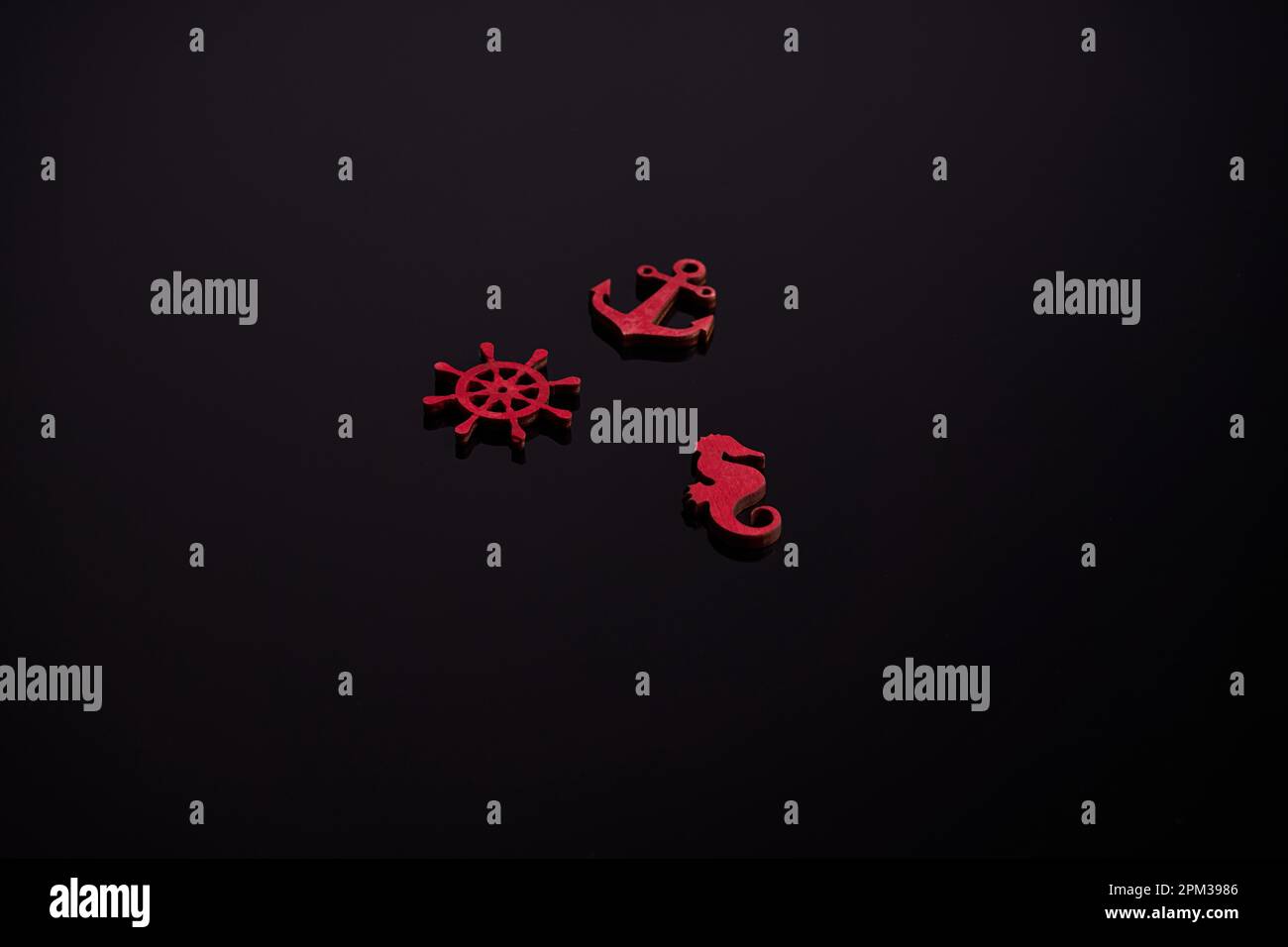 Un set di tre piccole statuine marine in legno rosso su sfondo nero. Foto Stock