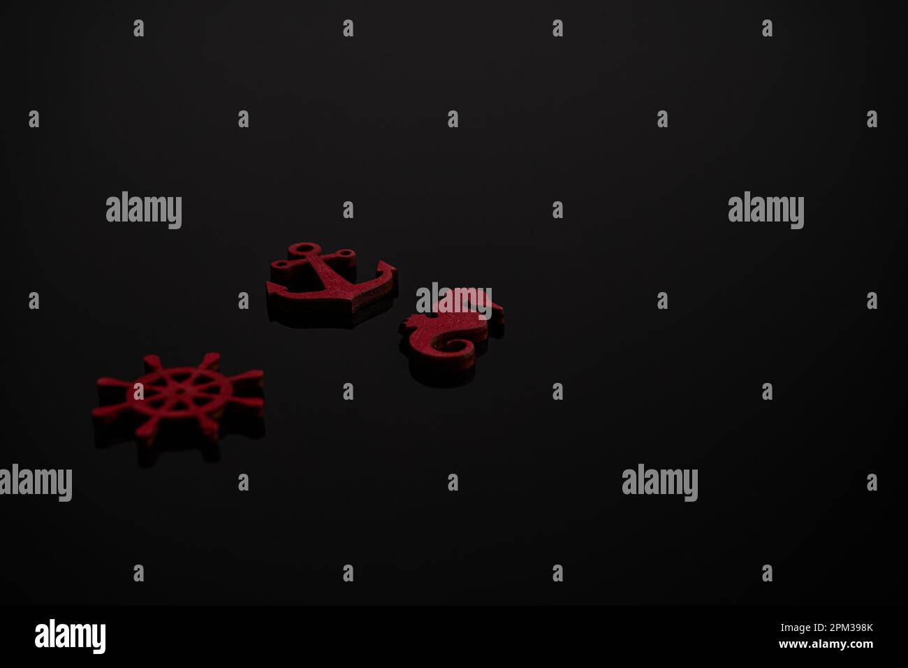 Un set di tre piccole statuine marine in legno rosso su sfondo nero. Foto Stock