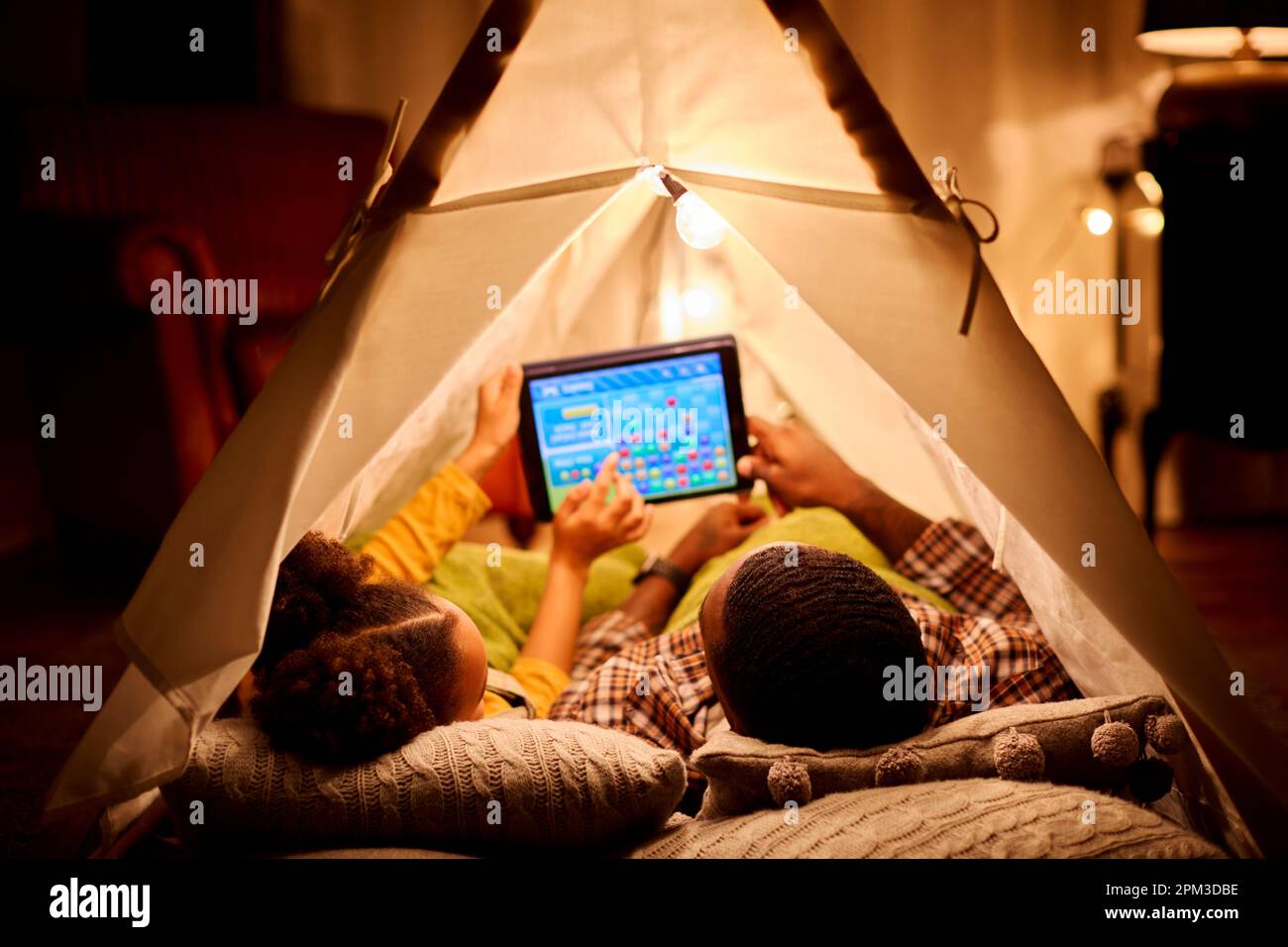 Padre e figlia a casa, sdraiati nella tenda interna o nel campo di gioco sul tablet digitale Foto Stock