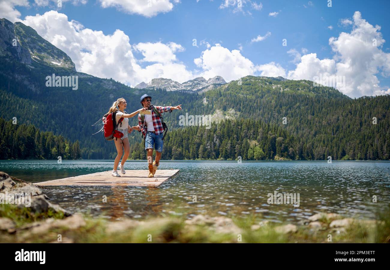 Giovane coppia avventurosa che tiene le mani ed eccitata sul molo di legno sul lago. Amore, escursioni, concetto di natura Foto Stock