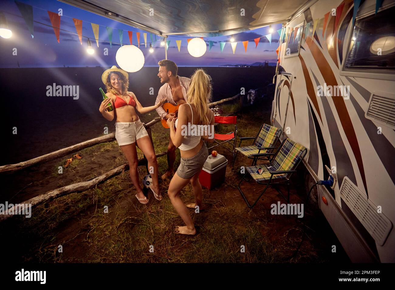 Gruppo di amici che hanno festa al tramonto sulla spiaggia; concetto di stile di vita informale Foto Stock