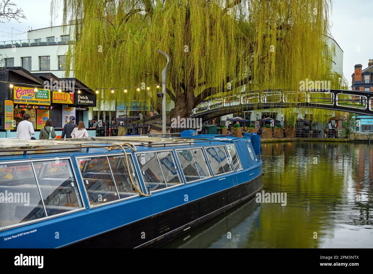 Camden Town, Londra, Regno Unito: Una barca sul Regents Canal vicino al Camden Market. Con un albero di salice, passerella, gente e punti di ristoro. Foto Stock