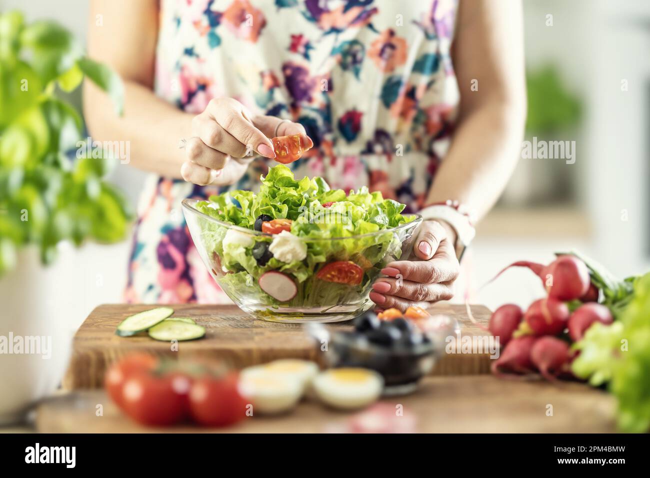 Una donna prepara un'insalata sana e mette un pomodoro a fette in una ciotola. Foto Stock