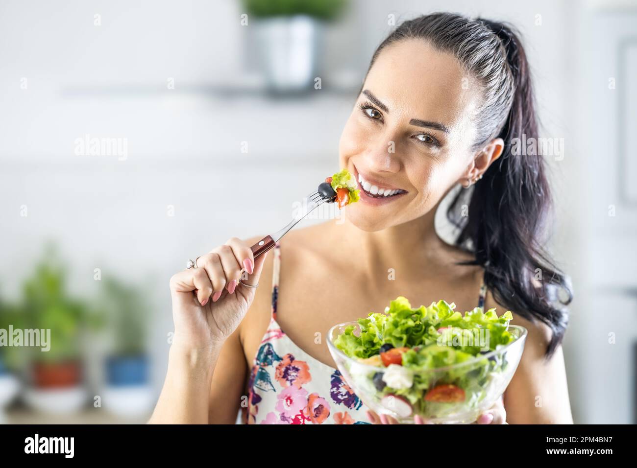 Stile di vita sano giovane donna che mangia insalata di lattuga. Giovane brunetta mangiare cibo sano in cucina. Foto Stock