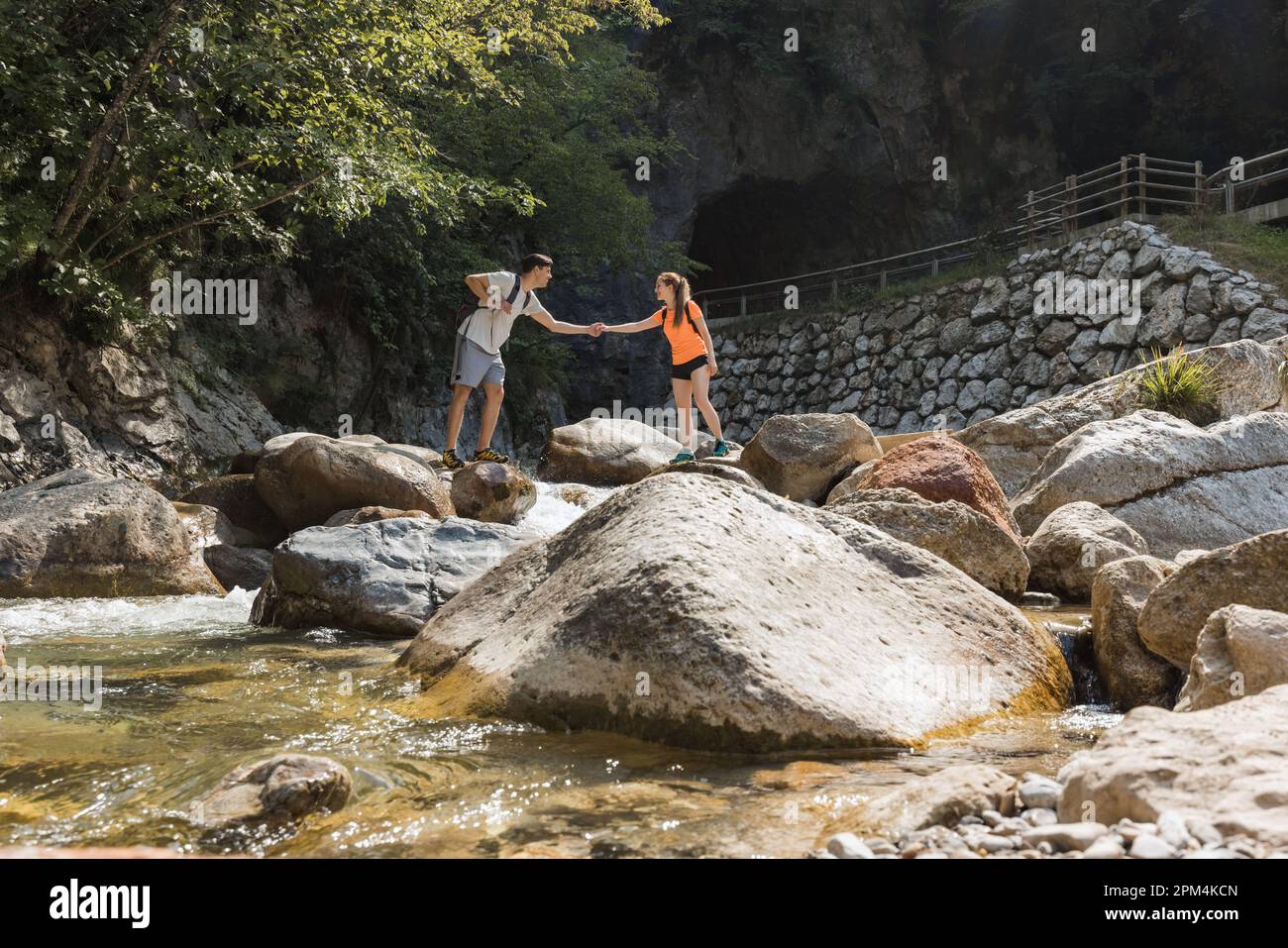 Coppia di escursionisti che cammina sulle rocce mentre attraversa il fiume di montagna, passando per un tour a piedi attraverso la gola. Concetto di stile di vita di viaggio e avventura. Foto Stock