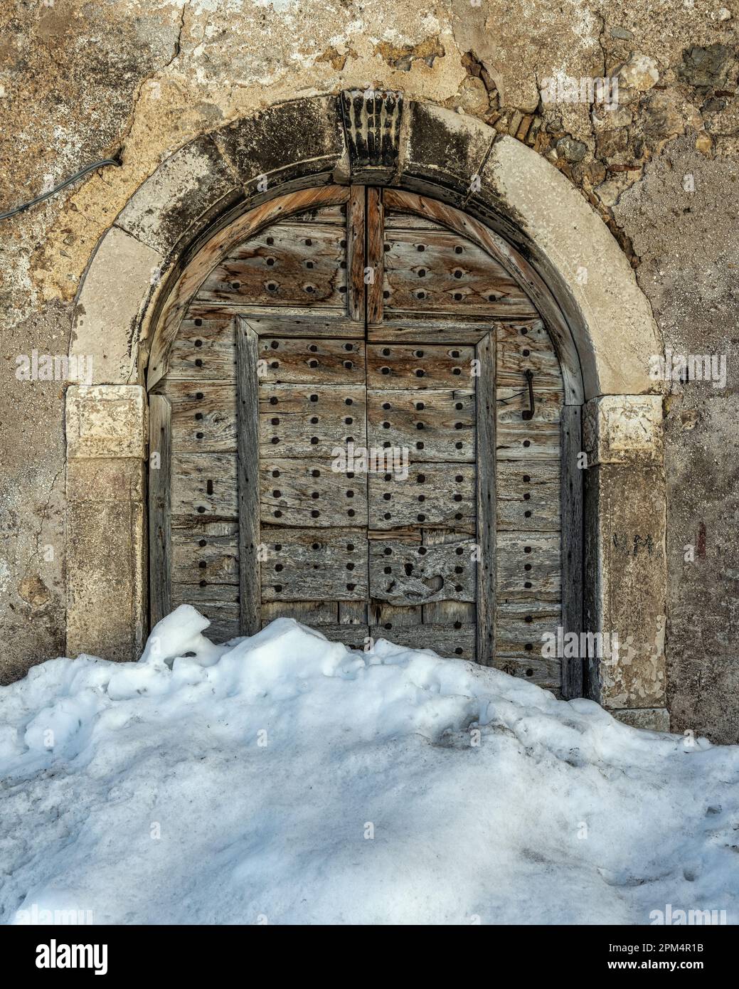 Antico portale con porte in legno bloccato da una nevicata nel piccolo borgo montano di campo di Giove. Parco Nazionale della Maiella, campo di Giove, Abruzzo Foto Stock