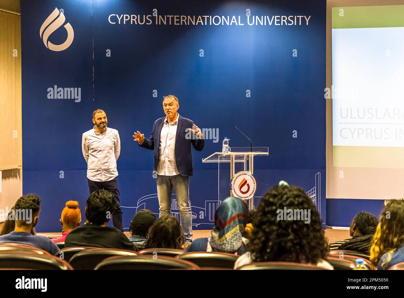 Due uomini parlano qui a studenti in un'aula dell'Università Internazionale di Cipro, fondata nel 1997, a Nicosia, Repubblica Turca di Cipro del Nord (RTNC); una proiezione con il nome dell'università in turco e inglese è visibile sullo sfondo. Foto Stock