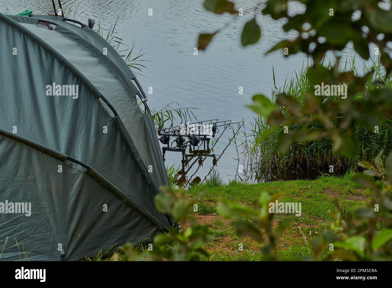 Pesca paesaggio immagine con rifugio da pesca e canne da pesca con un lago e qualche erba verde. Foto Stock