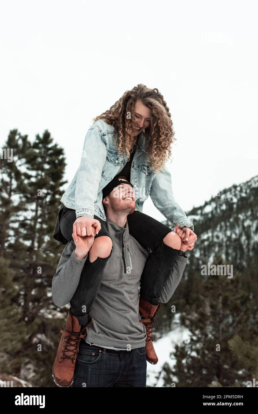 Giovane uomo che trasporta la donna sulle spalle in inverno nelle montagne del Colorado Foto Stock