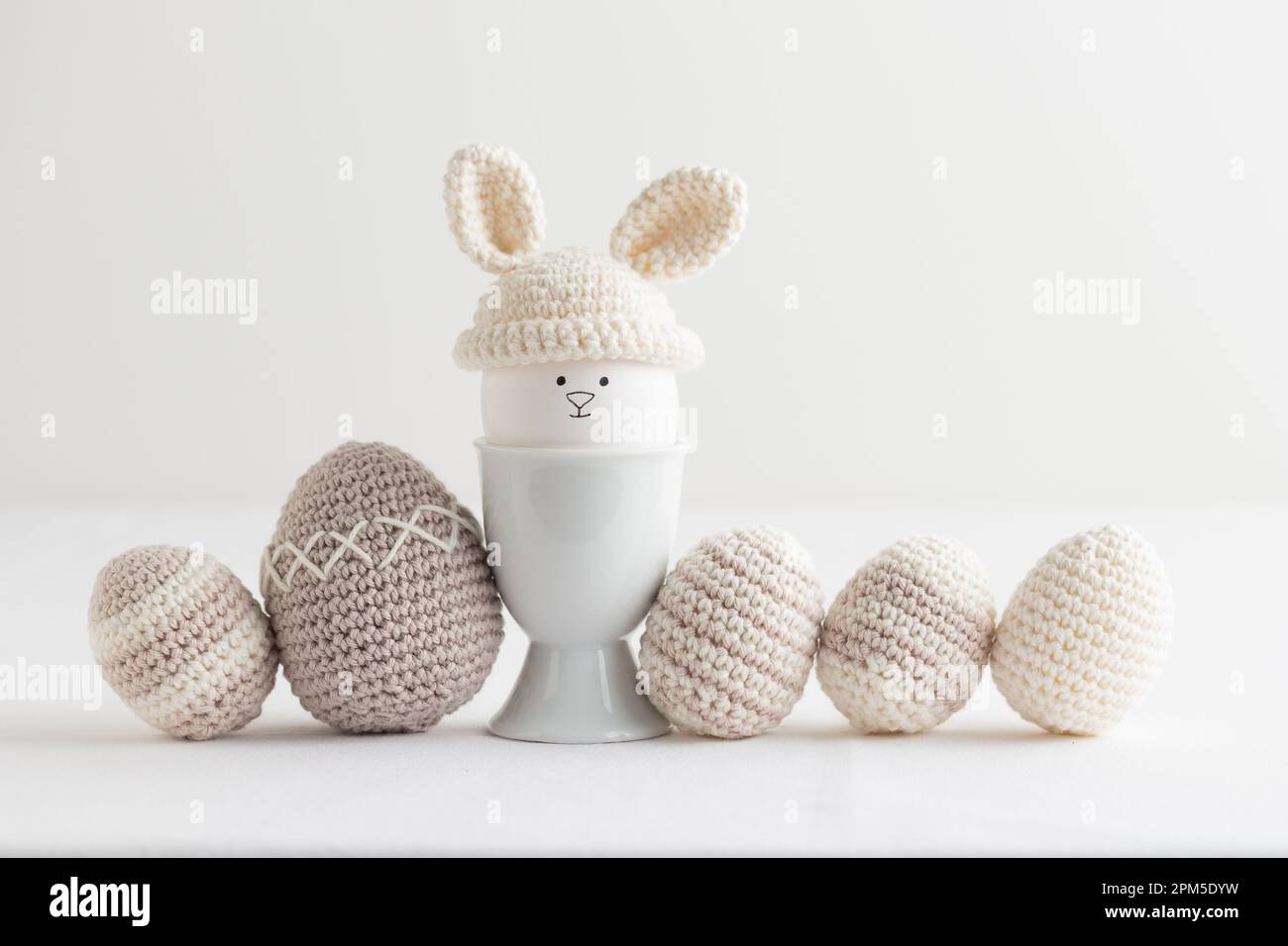 uovo di pasqua in cappello all'uncinetto con le orecchie da coniglio nel portuovo su bianco Foto Stock