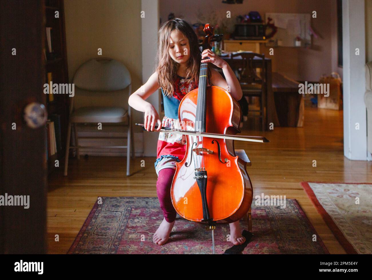 Una giovane ragazza a piedi nudi suona il violoncello appassionatamente con gli occhi chiusi Foto Stock