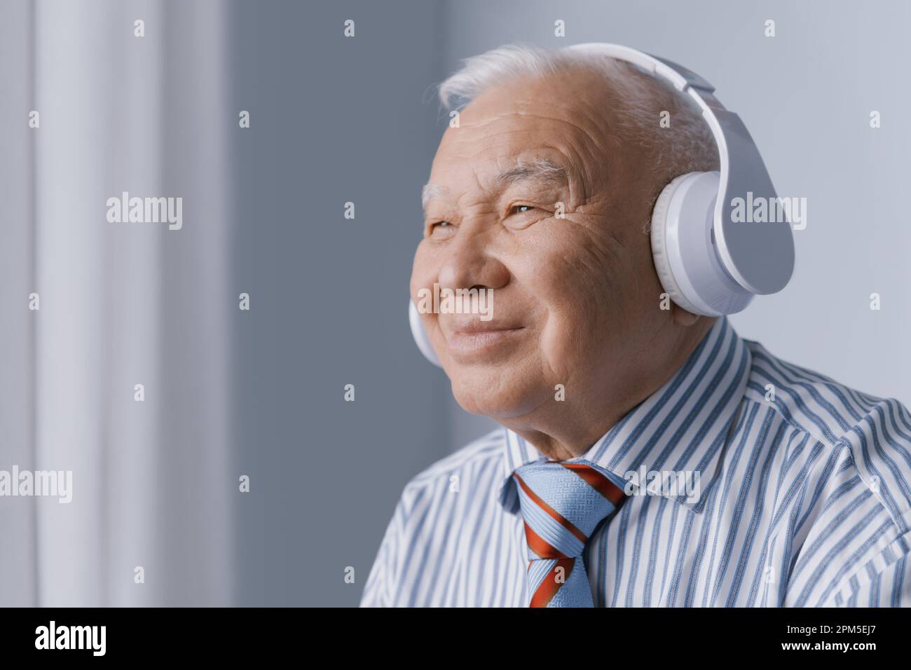 Un uomo d'affari anziano e sereno che indossa cuffie e ascolta l'audio Foto Stock