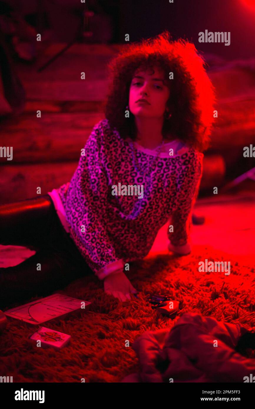 Ritratto di una giovane donna ricciola sdraiata su un tappeto rosso con pistole Foto Stock