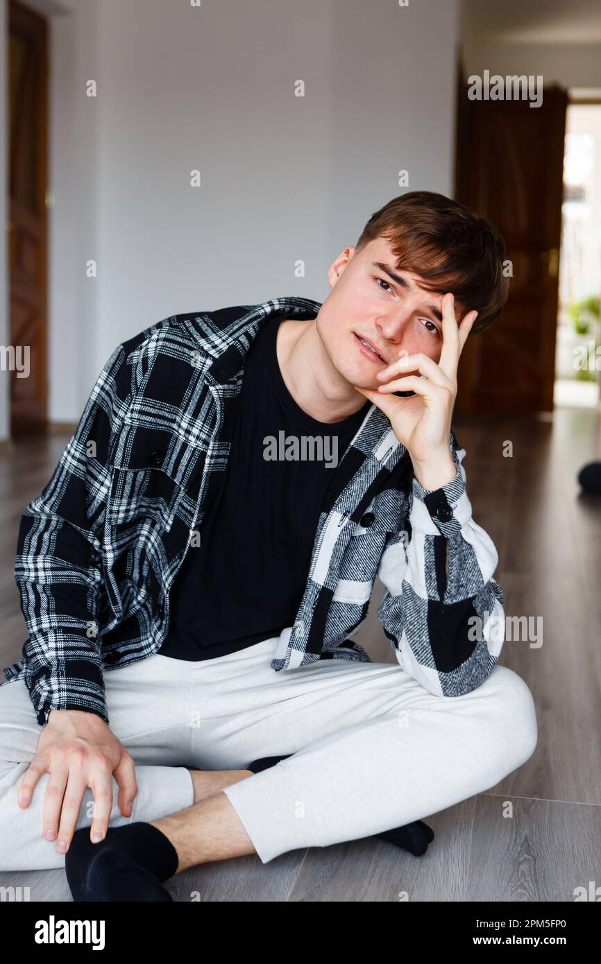 ragazzo seduto sul pavimento in vestiti di casa e guardando la macchina fotografica Foto Stock