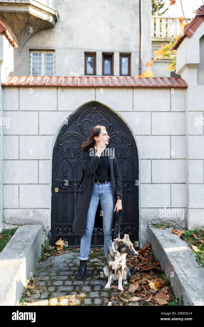 giovane donna in un cappotto con un cane in una passeggiata vicino alla casa Foto Stock