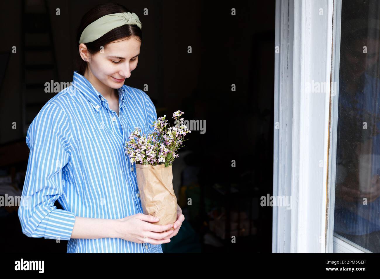 donna in camicia blu tiene il pacchetto di fiori nelle sue mani a casa Foto Stock