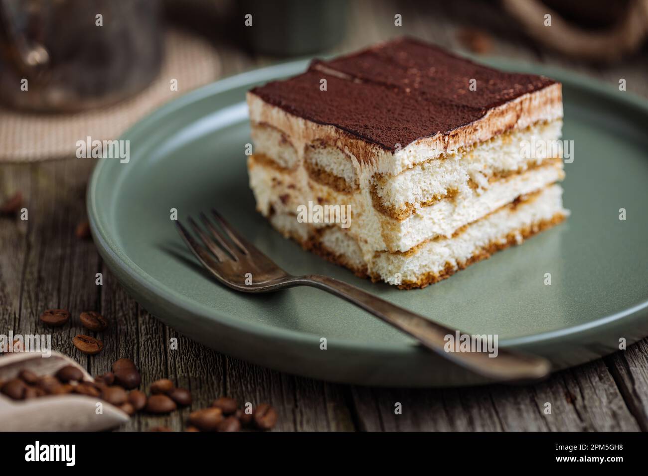 Un pezzo di torta tiramisù, dessert tradizionale italiano, servito in una scena rustica e piena di moody. Fondo in legno e piatto verde. Foto Stock