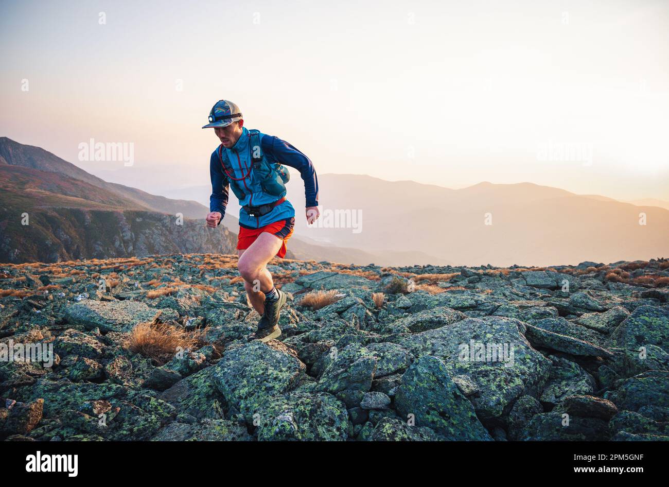 Corridore maschio che corre attraverso le rocce all'alba in montagna Foto Stock