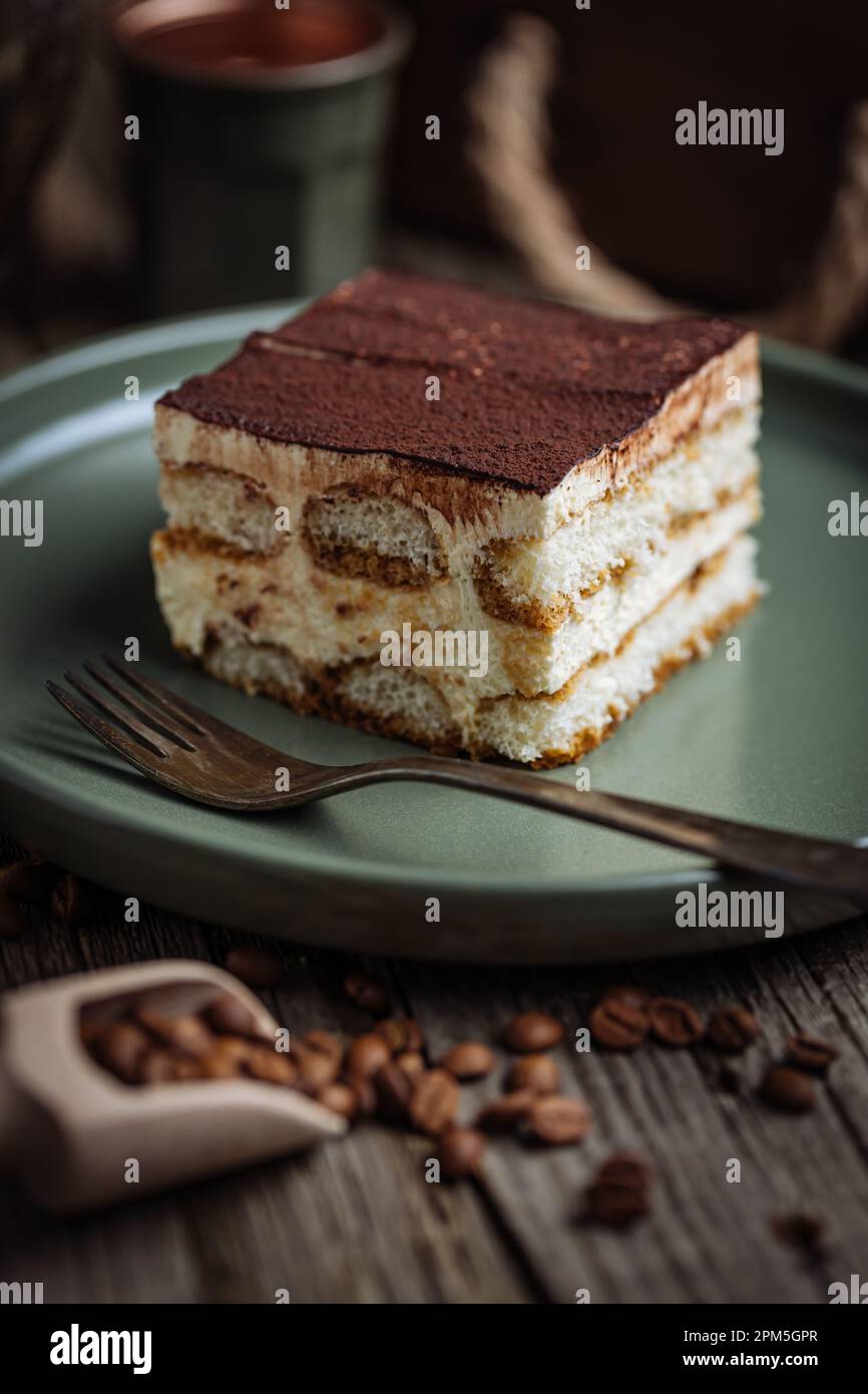 Un pezzo di torta tiramisù, dessert tradizionale italiano, servito in una scena rustica e piena di moody. Fondo in legno e piatto verde. Foto Stock