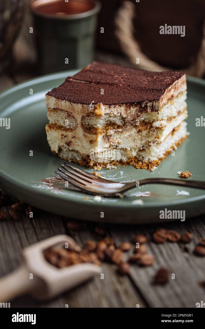 Un pezzo di torta tiramisù, dessert tradizionale italiano, servito in una scena rustica e piena di moody. Fondo in legno e piatto verde. Foto Stock