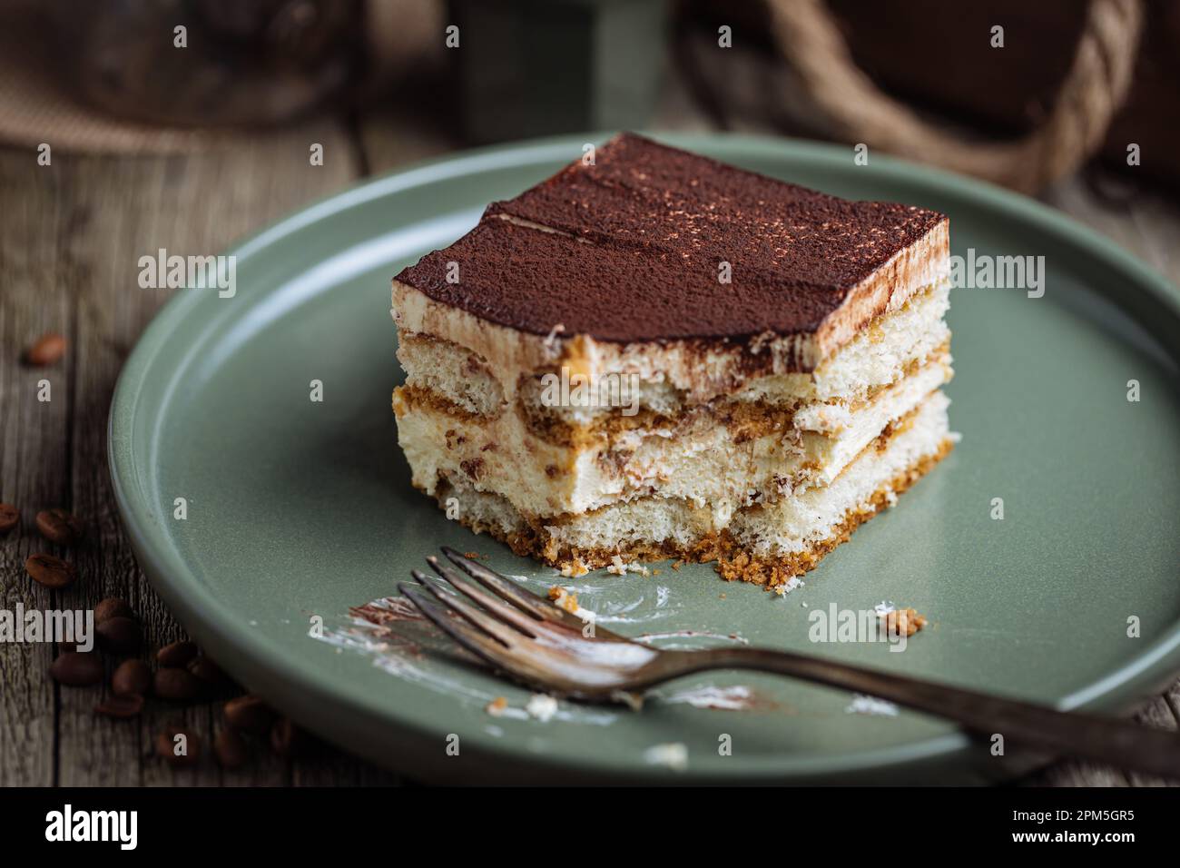 Un pezzo di torta tiramisù, dessert tradizionale italiano, servito in una scena rustica e piena di moody. Fondo in legno e piatto verde. Foto Stock