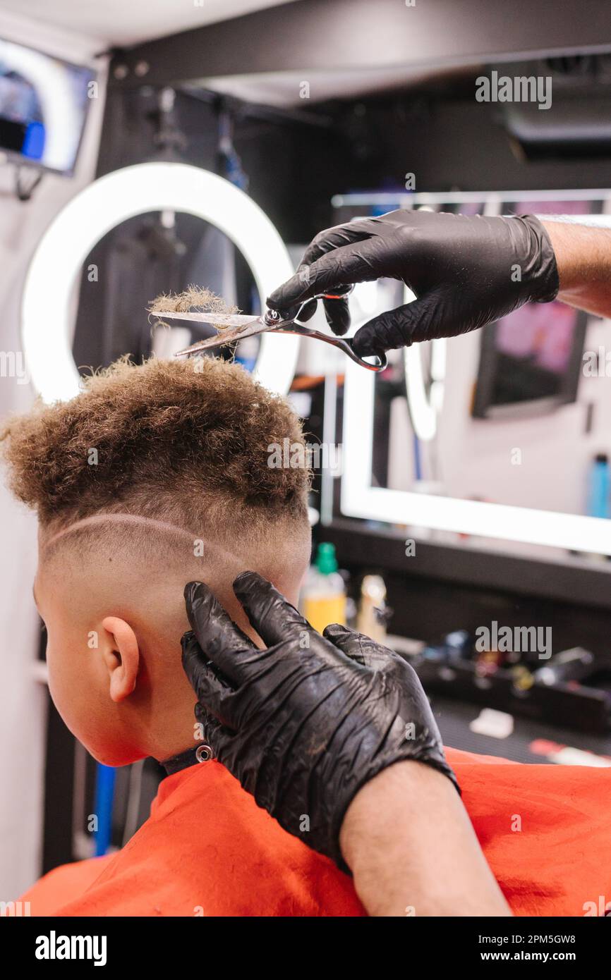 Sera barbiere latino fuori capelli ricci su ragazzo biraciale con forbici Foto Stock