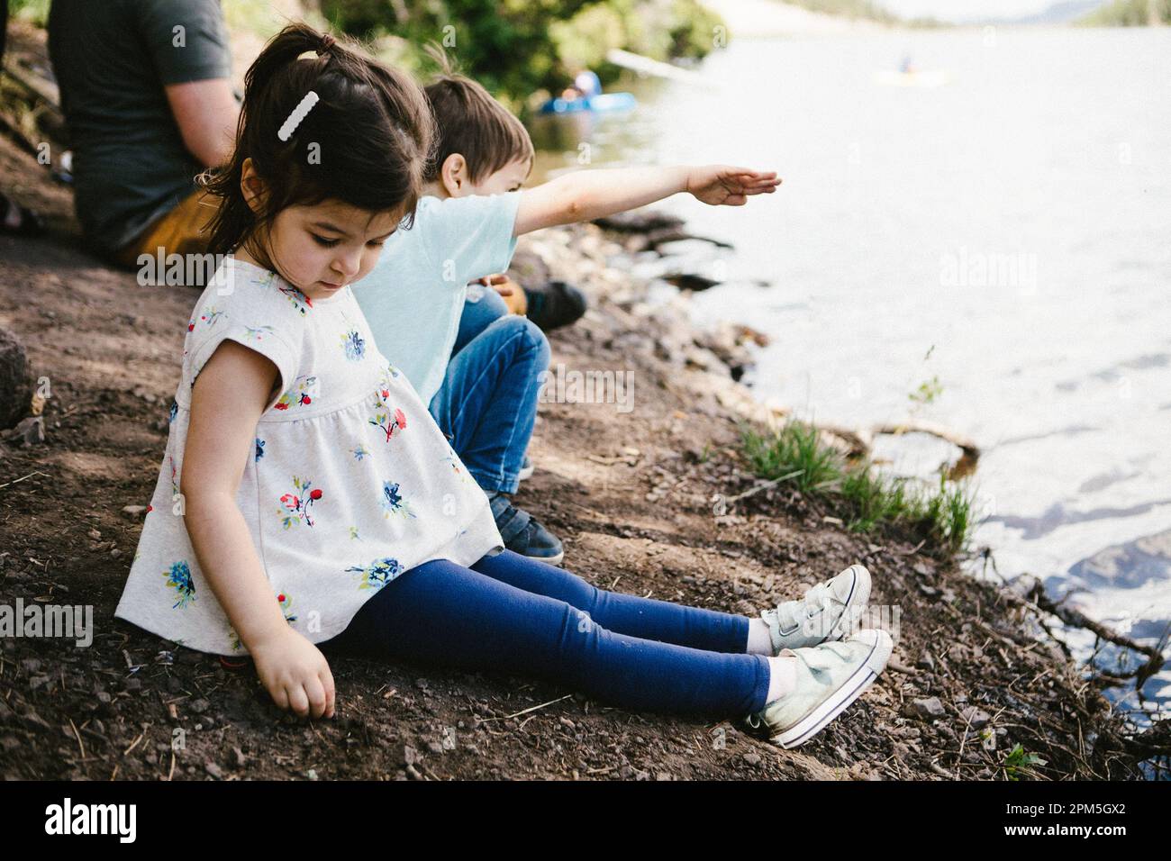 Bambina e ragazzo che si divertono sulla riva di un lago con la famiglia Foto Stock