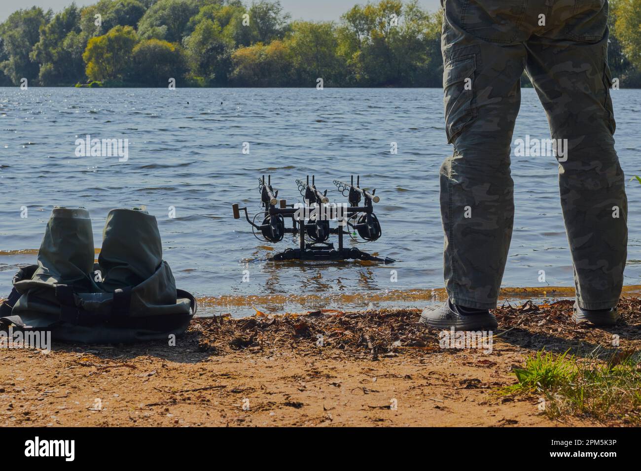 immagine paesaggistica di un lago con le canne di un pescatore nell'acqua e le gambe di un pescatore nell'immagine. Foto Stock
