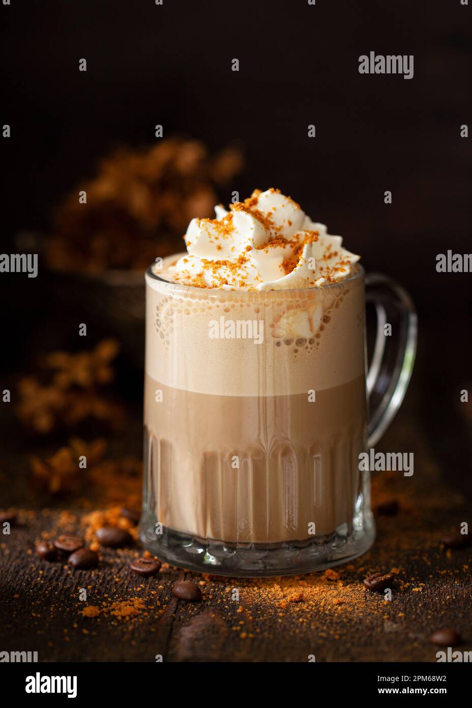 Una bevanda a base di caffè latte dolce con panna montata e biscotti sbriciolati in un ambiente rustico scuro e moody. Foto Stock