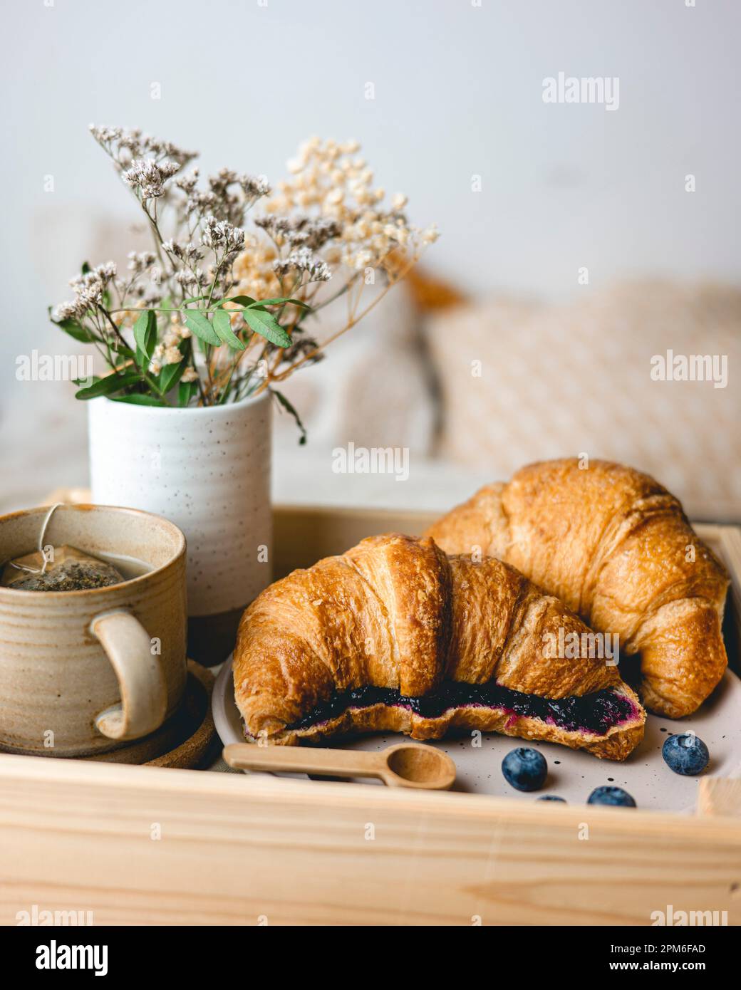 Prima colazione a letto con croissant appena sfornati con marmellata di mirtilli e tè in tazza. Foto Stock